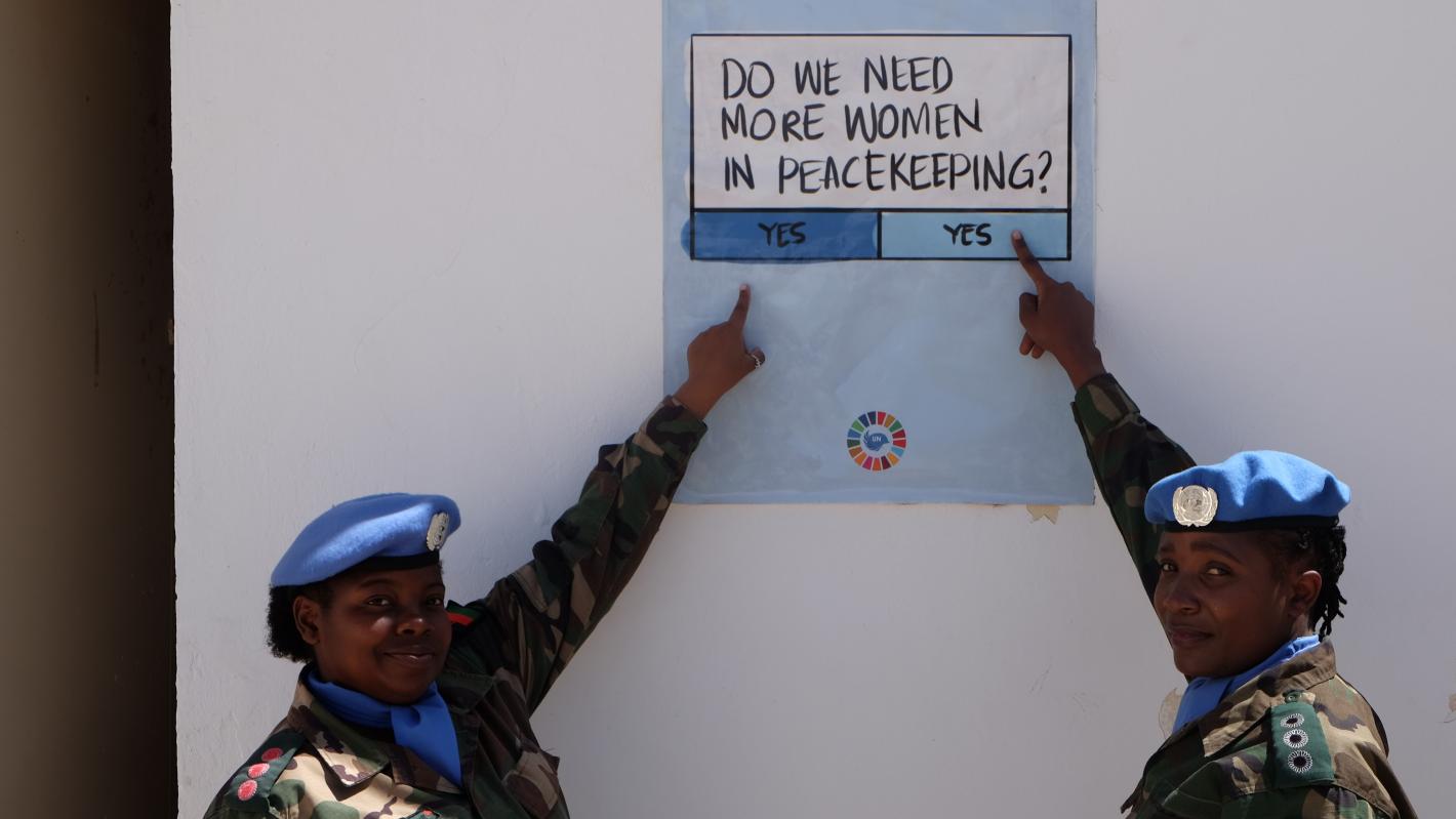 Do we need more women in peacekeeping? Yes or yes? Two women peacekeepers in military uniform point at a sign that poses the question "do we need more women in peacekeeping" and gives "yes" or "yes" as possible responses.