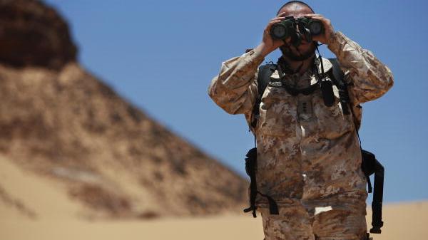 UN Photo/Martine Perret A UN peacekeeper in sand-coloured military uniform stands in the desert looking through binoculars