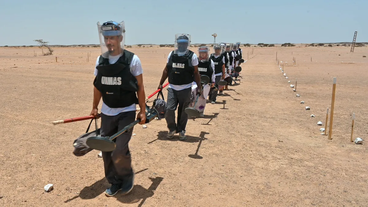 A line of UN de-miners in safety equipment walk through the desert