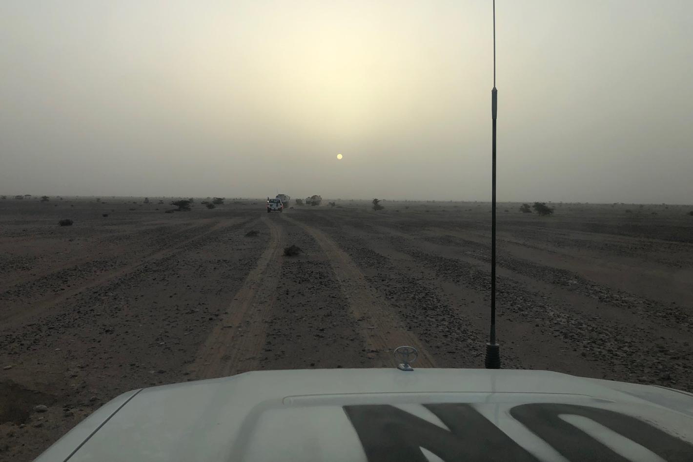 A vehicle marked UN drives along a desert road at sunset