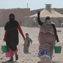 Two women carrying green buckets with a young child following behind them