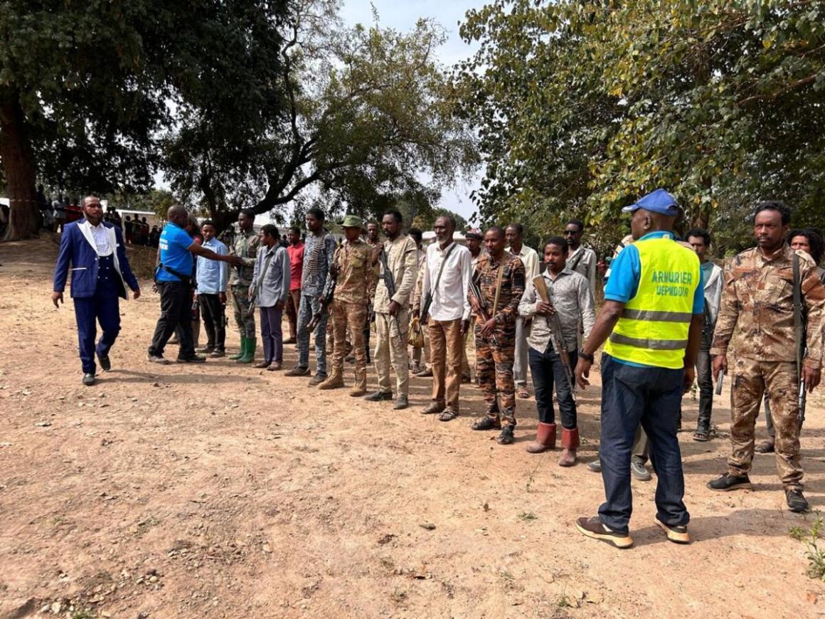 Des hommes en uniforme militaire et en tenue civile se tiennent en ligne, certains tenant des armes.