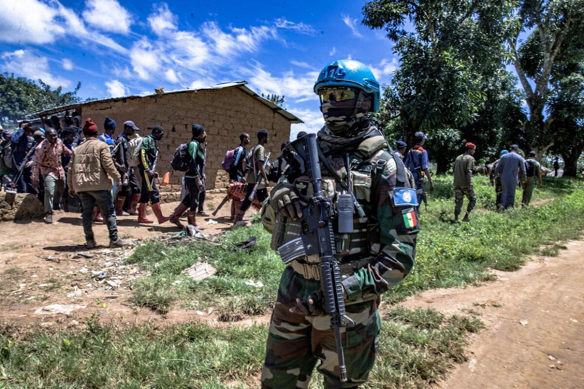 A UN Peacekeeper stands guard near a line of people.